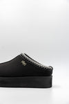 Black slip-on shoe with white stitching on a light gray background